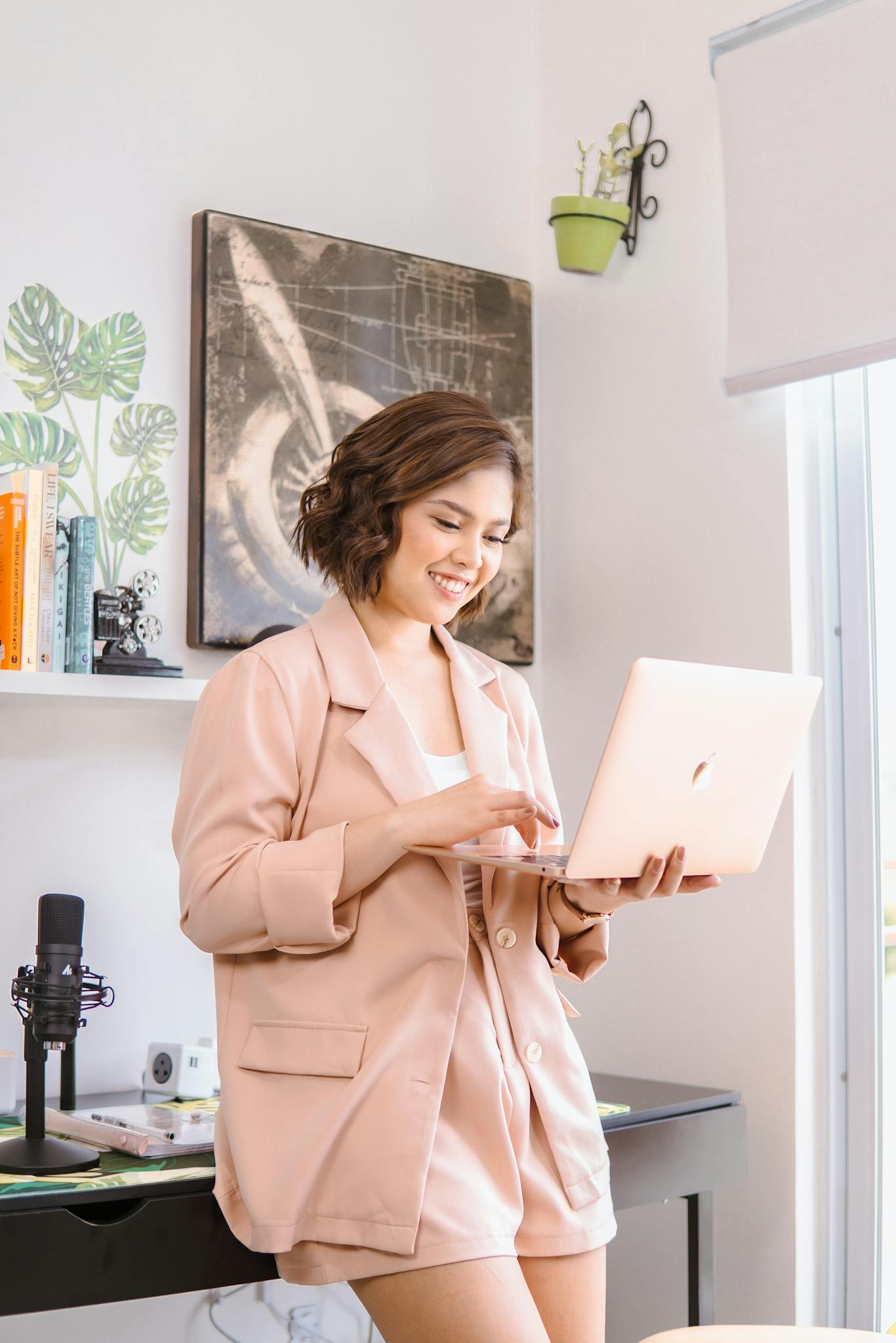 Smiling woman in trendy pink outfit using laptop in modern home office setting